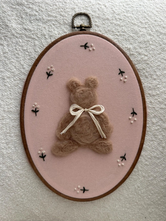 Embroidery hoop with a teddy bear and bow on a pink background