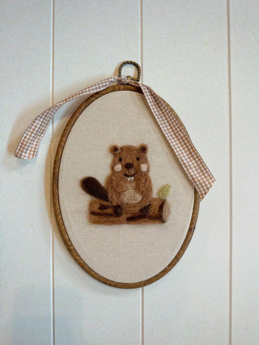 Embroidery of a beaver in an oval frame with a checkered ribbon on a wooden panel background