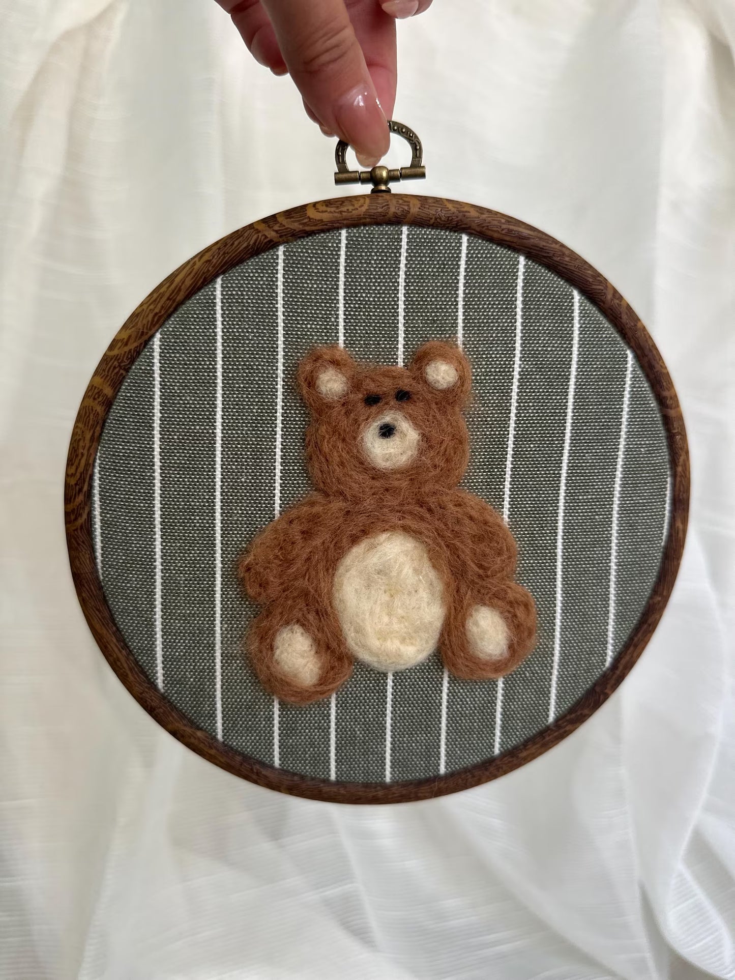 Felted teddy bear in a wooden embroidery hoop against a striped background
