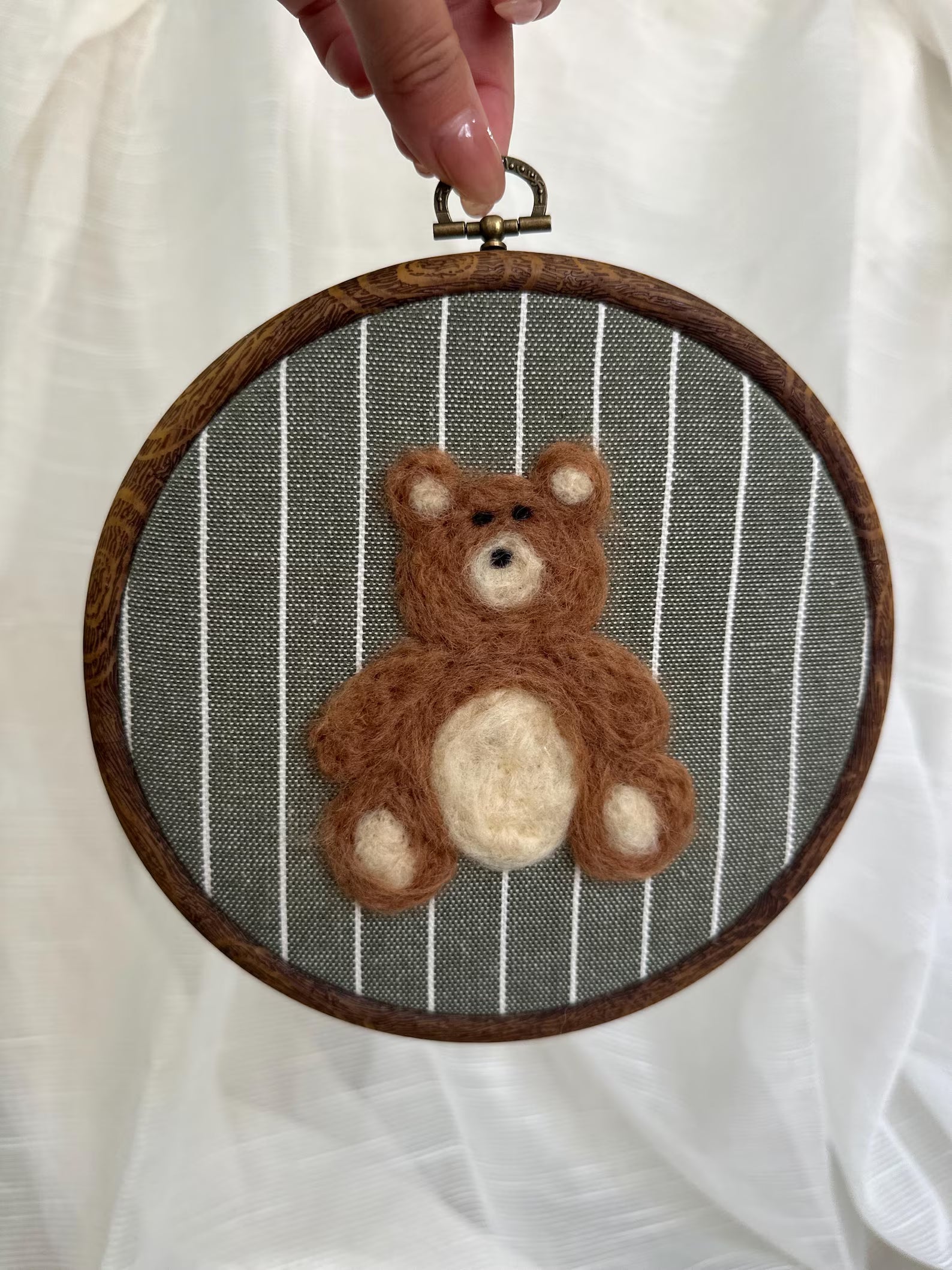Felted teddy bear in a wooden embroidery hoop against a striped background