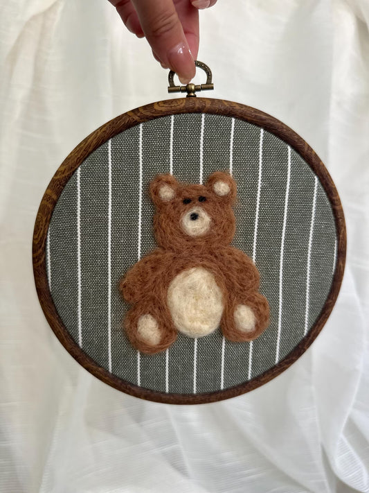 Felted teddy bear in a wooden embroidery hoop against a striped background