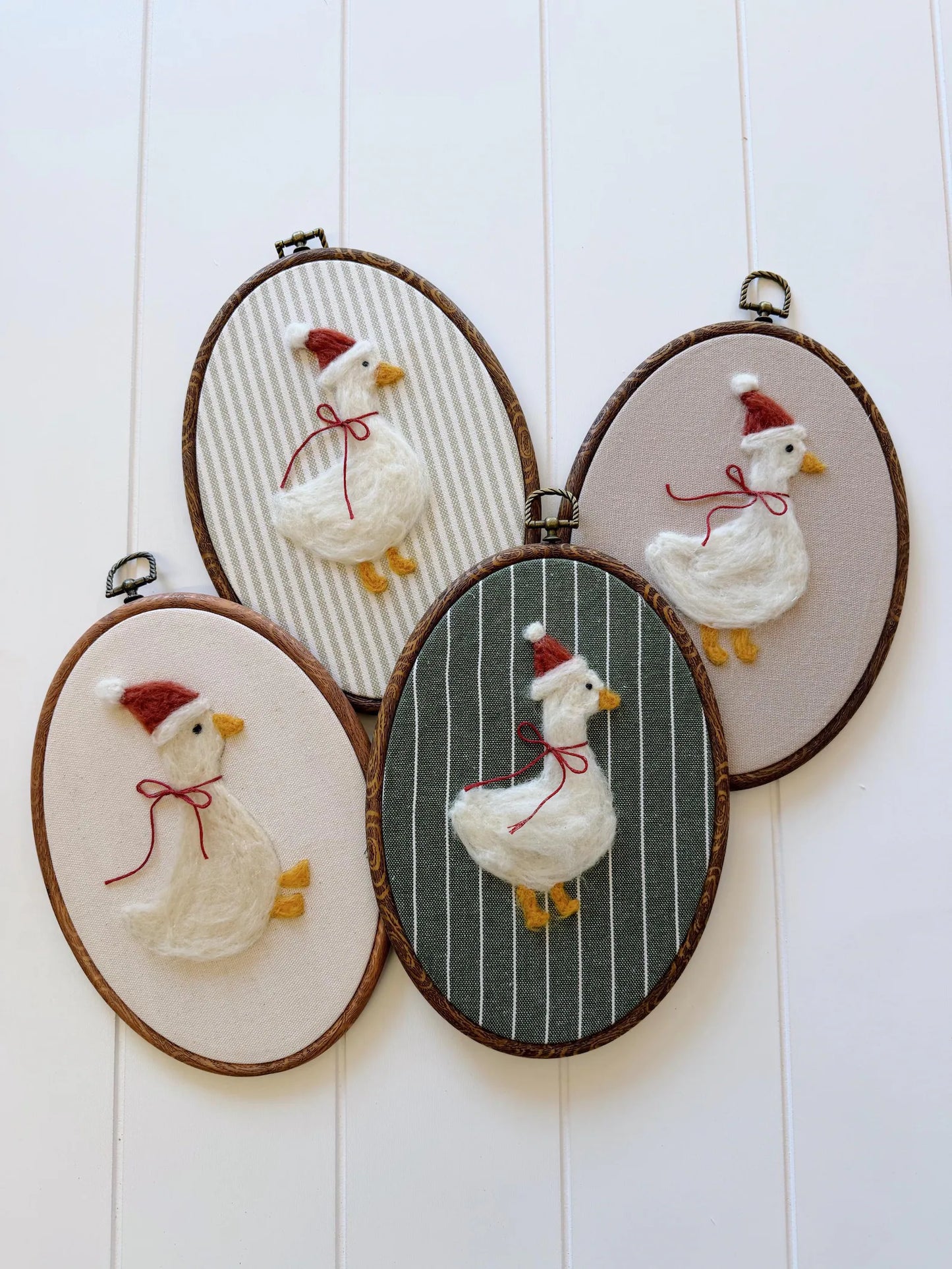 Set of four embroidered hoop art pieces featuring geese with red bows on a white wooden background.