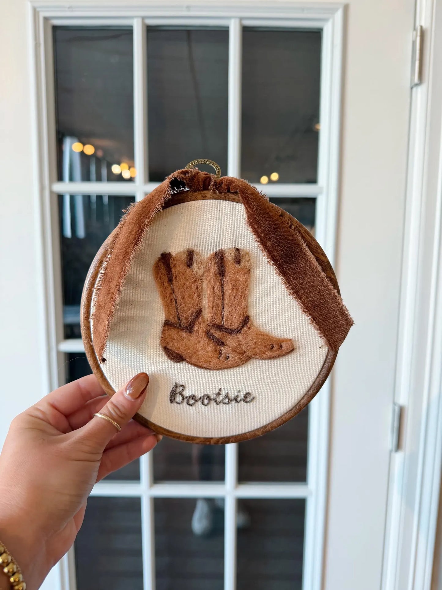 Decorative ornament with cowboy boots and 'Bootsie' text held by a hand.
