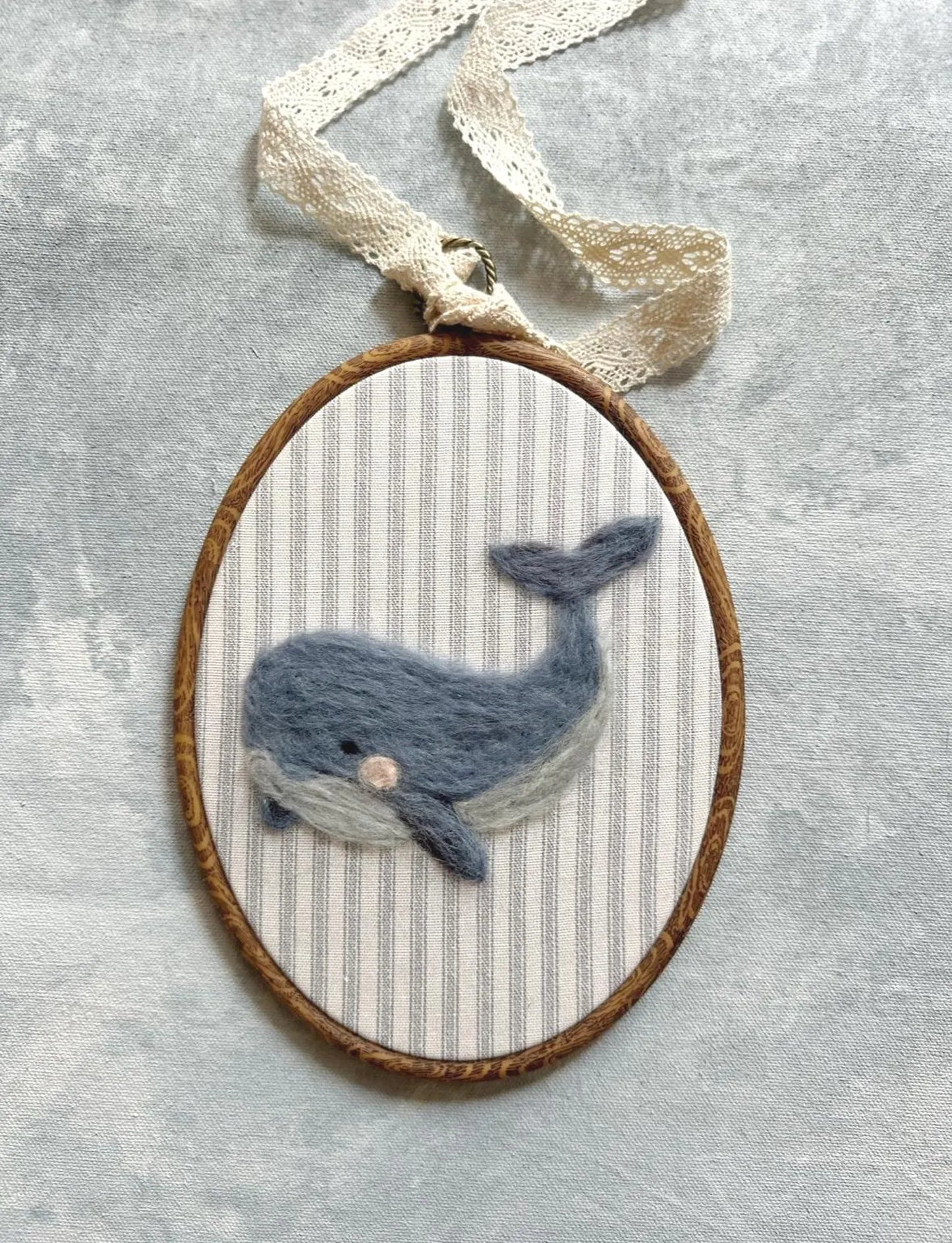 Felted whale in a wooden hoop on a textured gray background