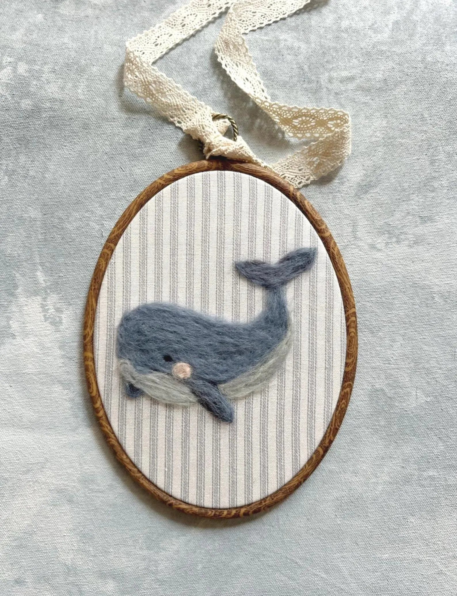 Felted whale in a wooden hoop on a textured gray background