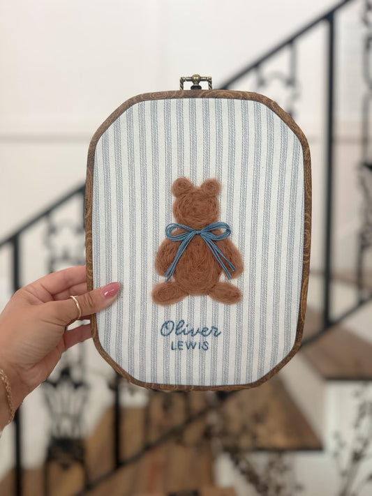 Embroidery hoop with a teddy bear design and 'Oliver Lewis' text, held by a hand.