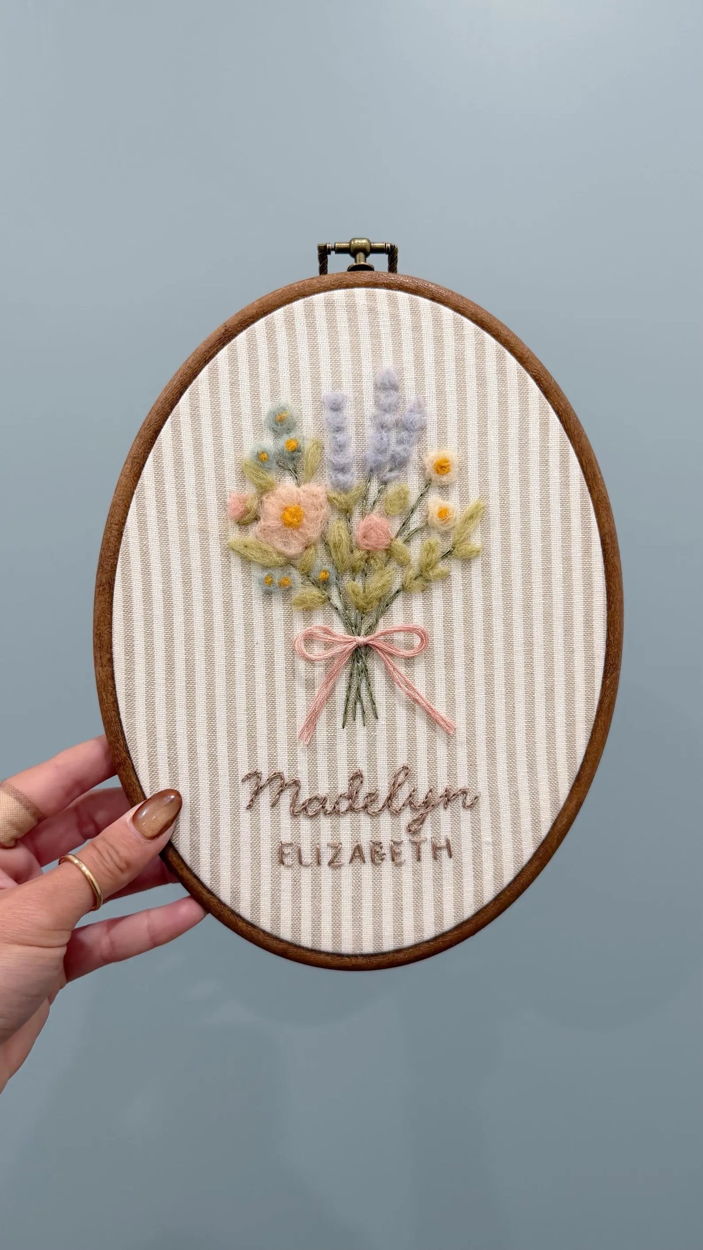 Embroidery hoop with floral design and text held against a gray background