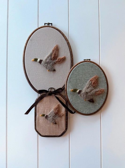 Three embroidered hoop art pieces of mallard ducks on a white wooden panel background