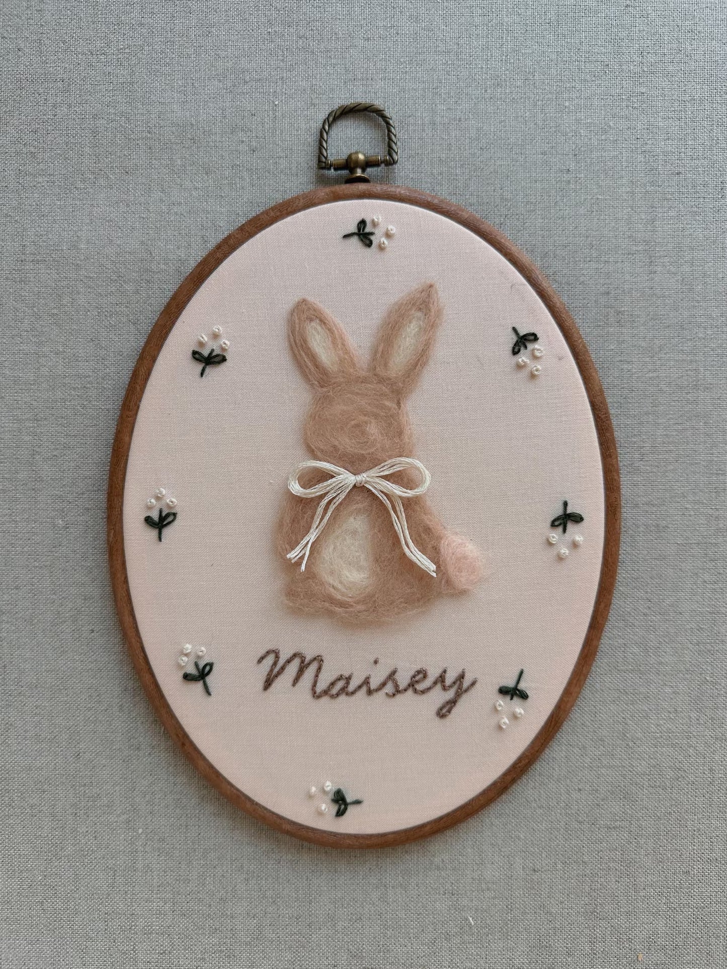 Embroidery hoop with a rabbit design and 'Maisy' text on a gray background