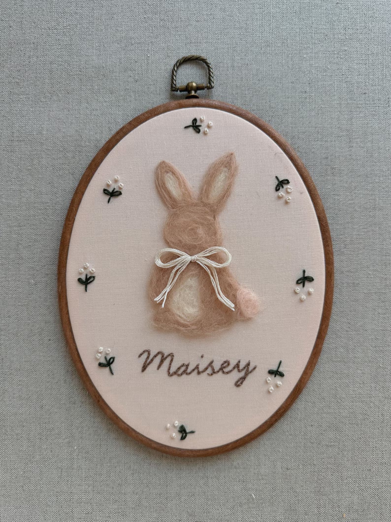 Embroidery hoop with a rabbit design and 'Maisy' text on a gray background