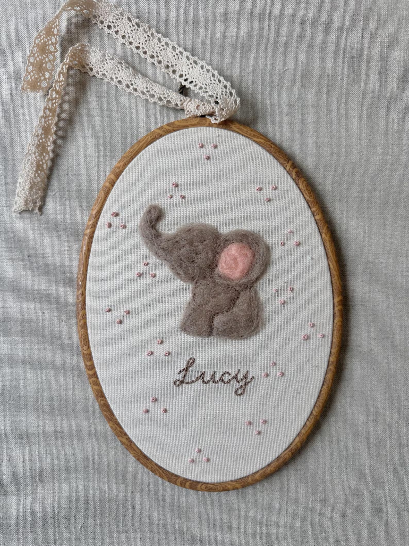 Embroidery hoop with a felted elephant design and the name 'Lucy' on a gray background.