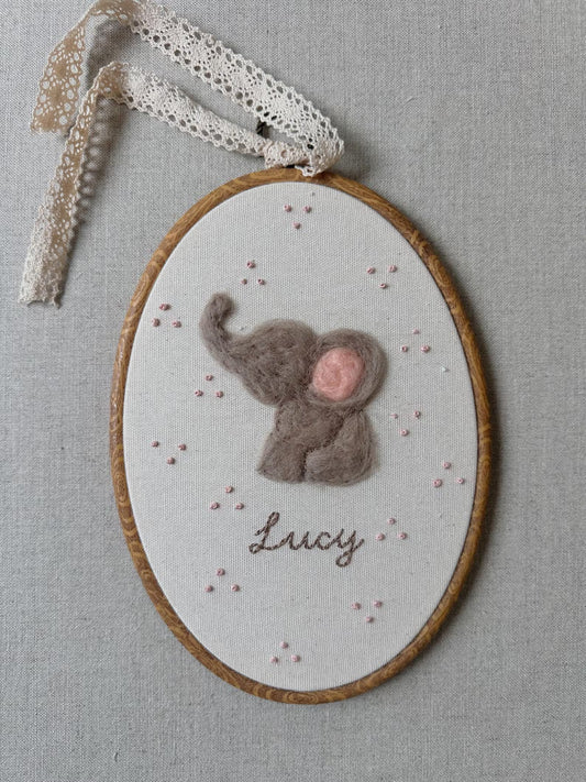 Embroidery hoop with a felted elephant design and the name 'Lucy' on a gray background.