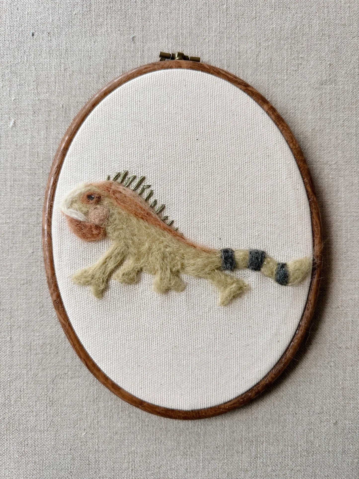 Embroidered lizard on a white fabric background inside a wooden hoop.