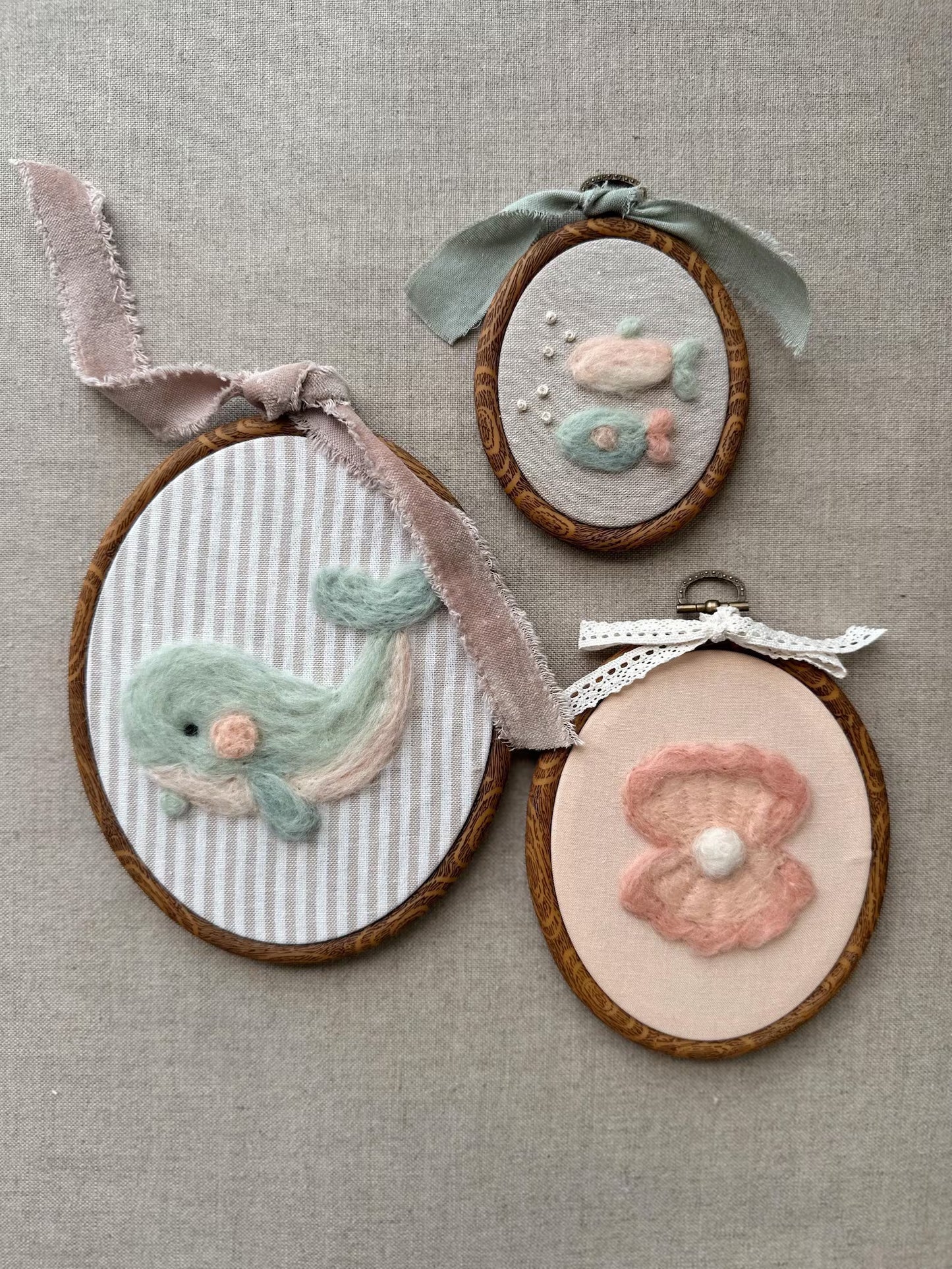Three embroidered hoop art pieces on a textured fabric background