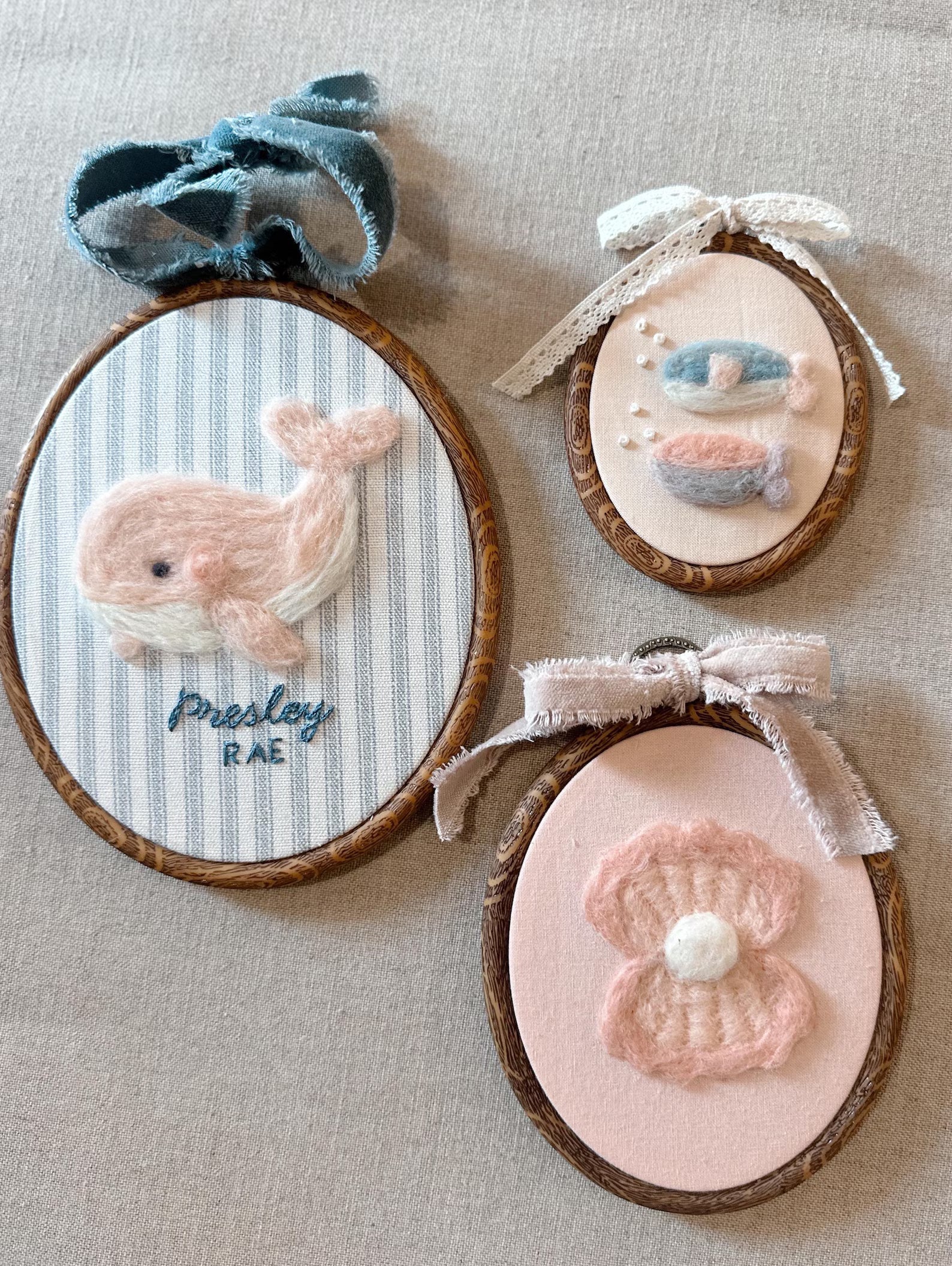 Three embroidered hoop art pieces with whale, fish, and flower designs on a beige fabric background.