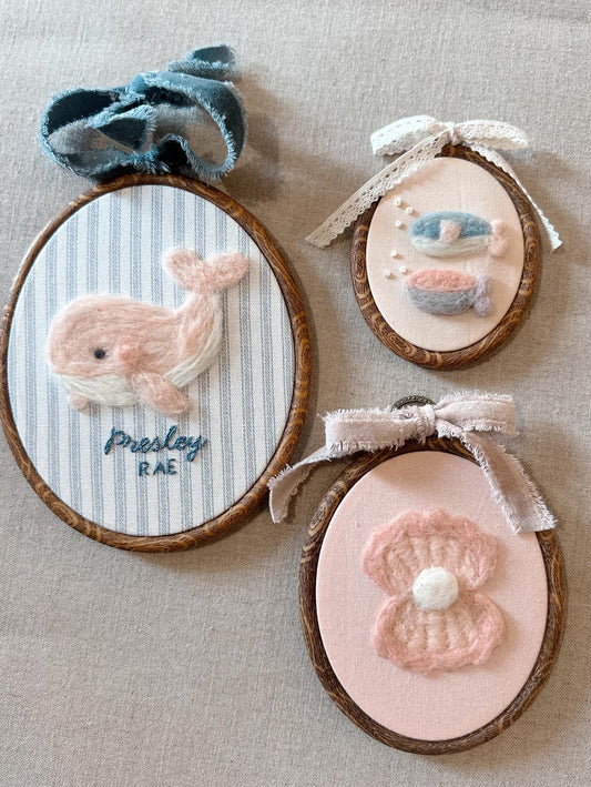 Three embroidered hoop art pieces with whale, fish, and flower designs on a beige fabric background.