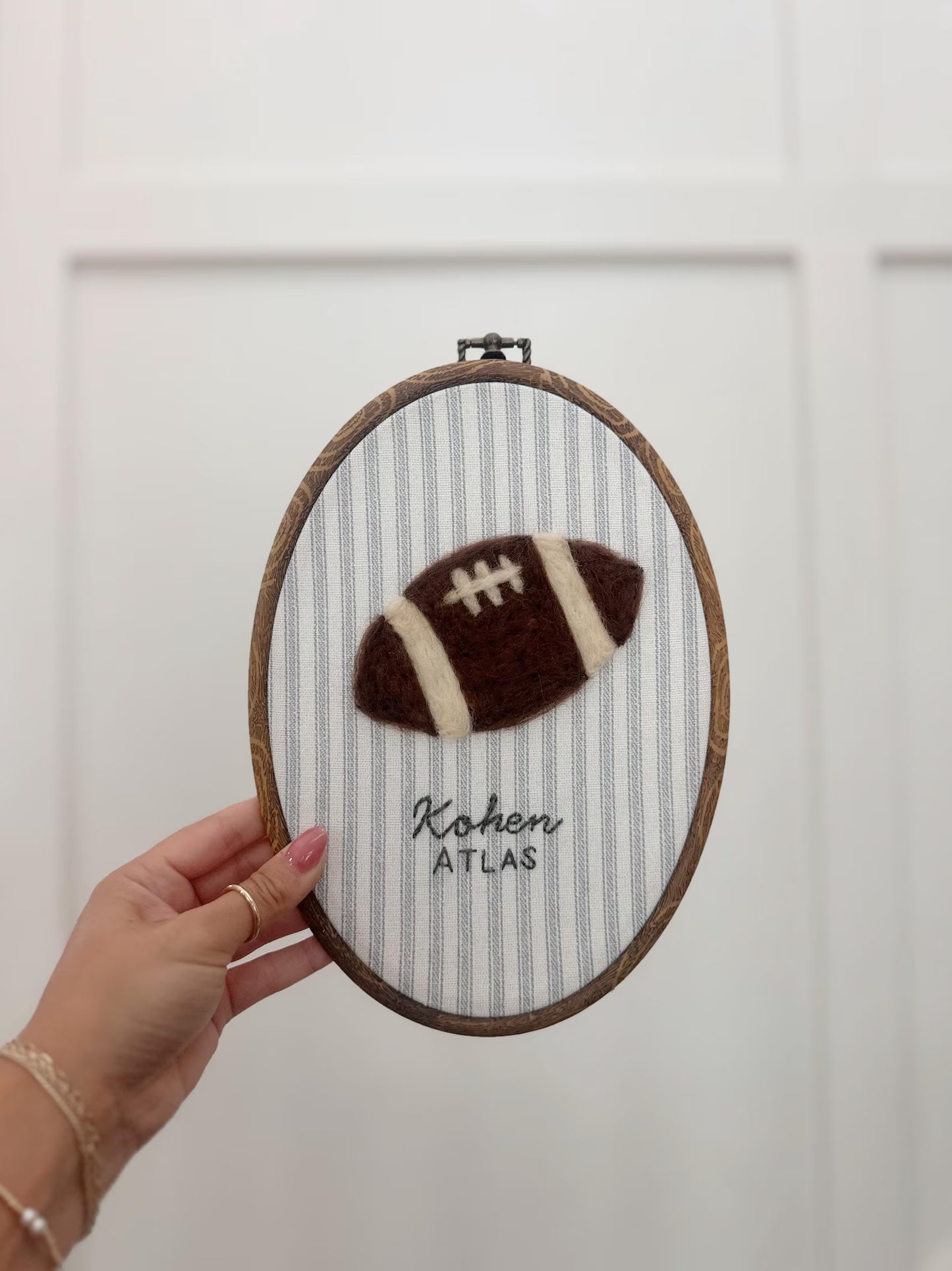 Embroidery hoop with a football design and text held by a hand against a white background